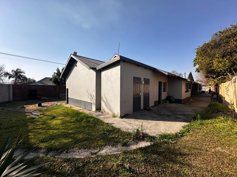 Rear view of the house featuring a concrete patio area, plastered exterior walls, and a metal roof, set within a private backyard.