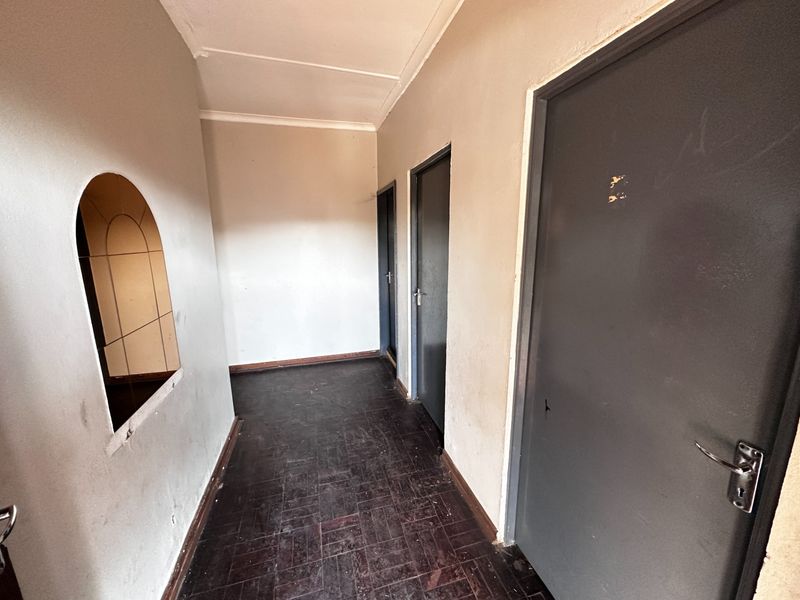 A vacant hallway featuring dark parquet flooring, an arched wall opening, and multiple internal doors, requiring cosmetic updates to improve its overall condition.