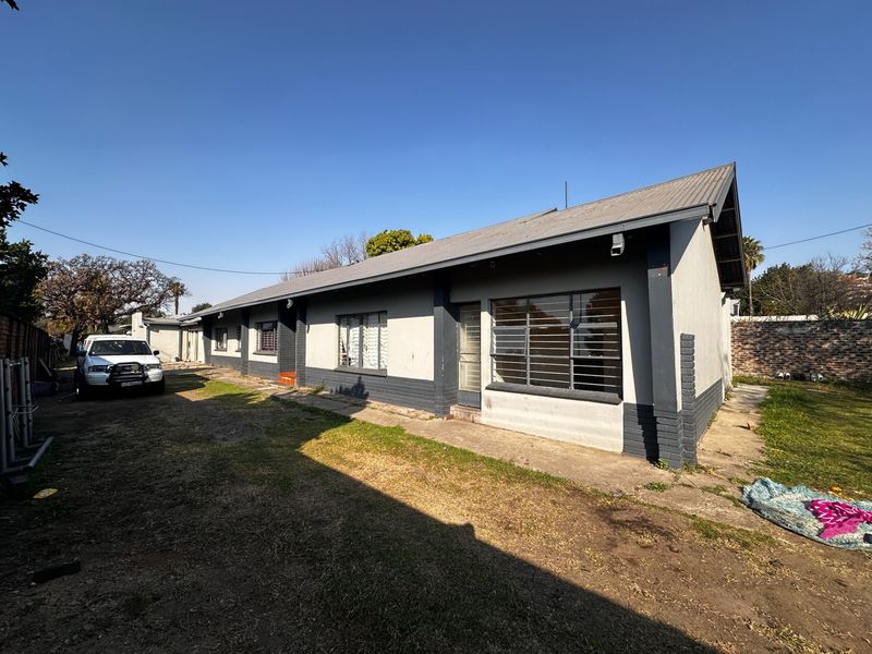 Rear view of the house featuring a corrugated metal roof, security-barred windows, and a surrounding garden area with a concrete walkway.