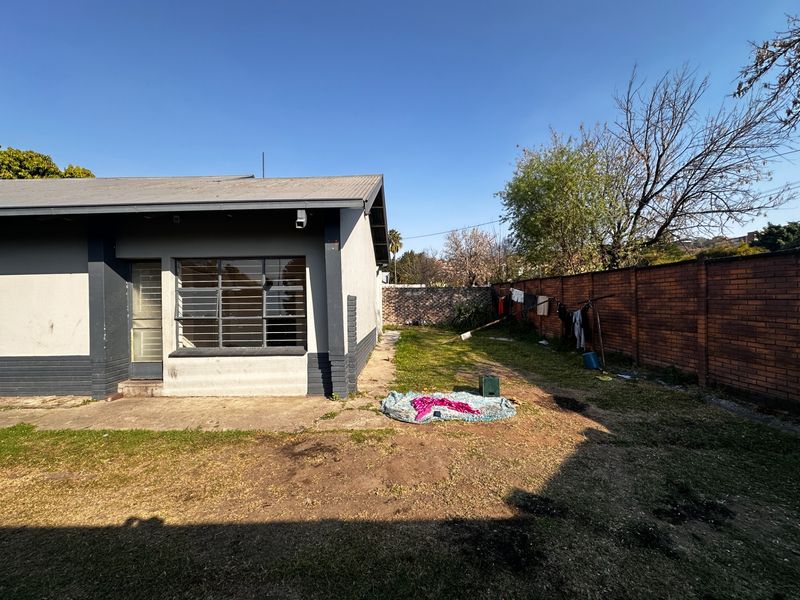 Rear view of the property featuring a brick boundary wall, metal-framed windows with security bars, and a concrete patio area leading to the garden.