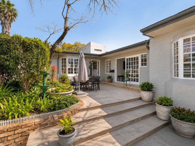 A well-maintained paved patio area featuring brick garden borders, mature landscaping, and direct access to the home through sliding glass doors.
