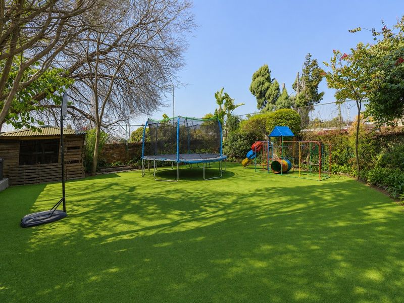 A well-maintained backyard featuring artificial turf, a wooden storage shed, and established perimeter landscaping with brick and chain link boundary walls.