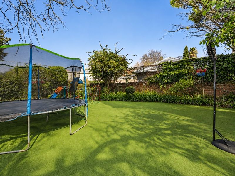 A well-maintained private garden featuring an artificial lawn, mature perimeter greenery, and a solid brick boundary wall.