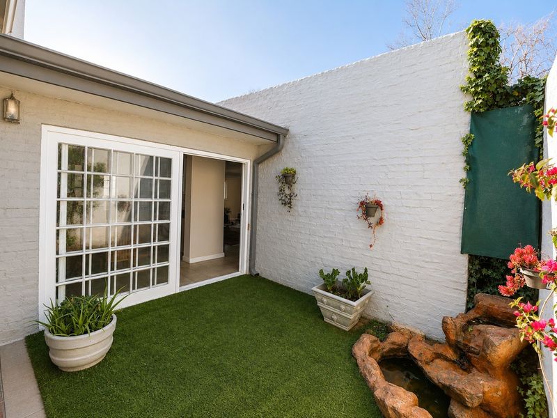 A private rear courtyard featuring artificial turf, a decorative water feature, and a sliding glass door providing access to the interior living space.