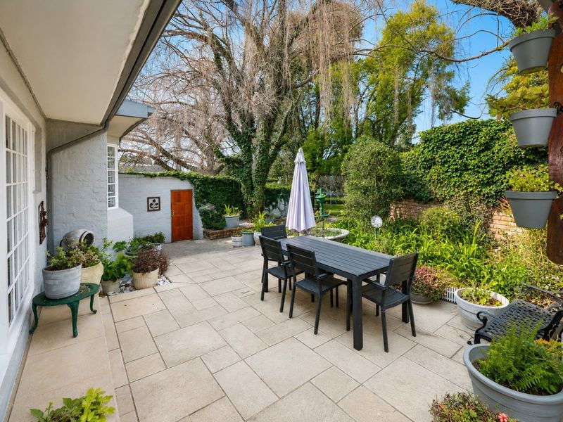 A well-maintained paved patio area featuring a brick boundary wall and established garden surroundings, ideal for outdoor dining and relaxation.