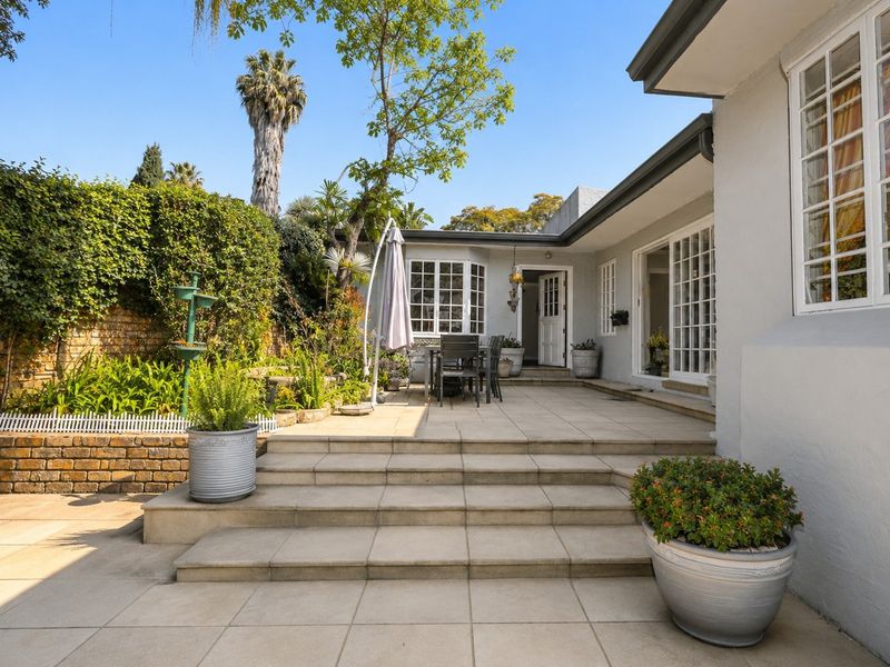 A well-maintained rear patio area featuring tiled flooring, stone steps, and direct access to the home through sliding glass doors and a garden entrance.