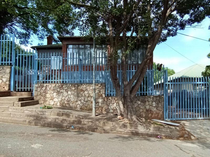 Front elevation of the property featuring a stone retaining wall, concrete stairs, and blue steel security fencing surrounding the brick-built house.