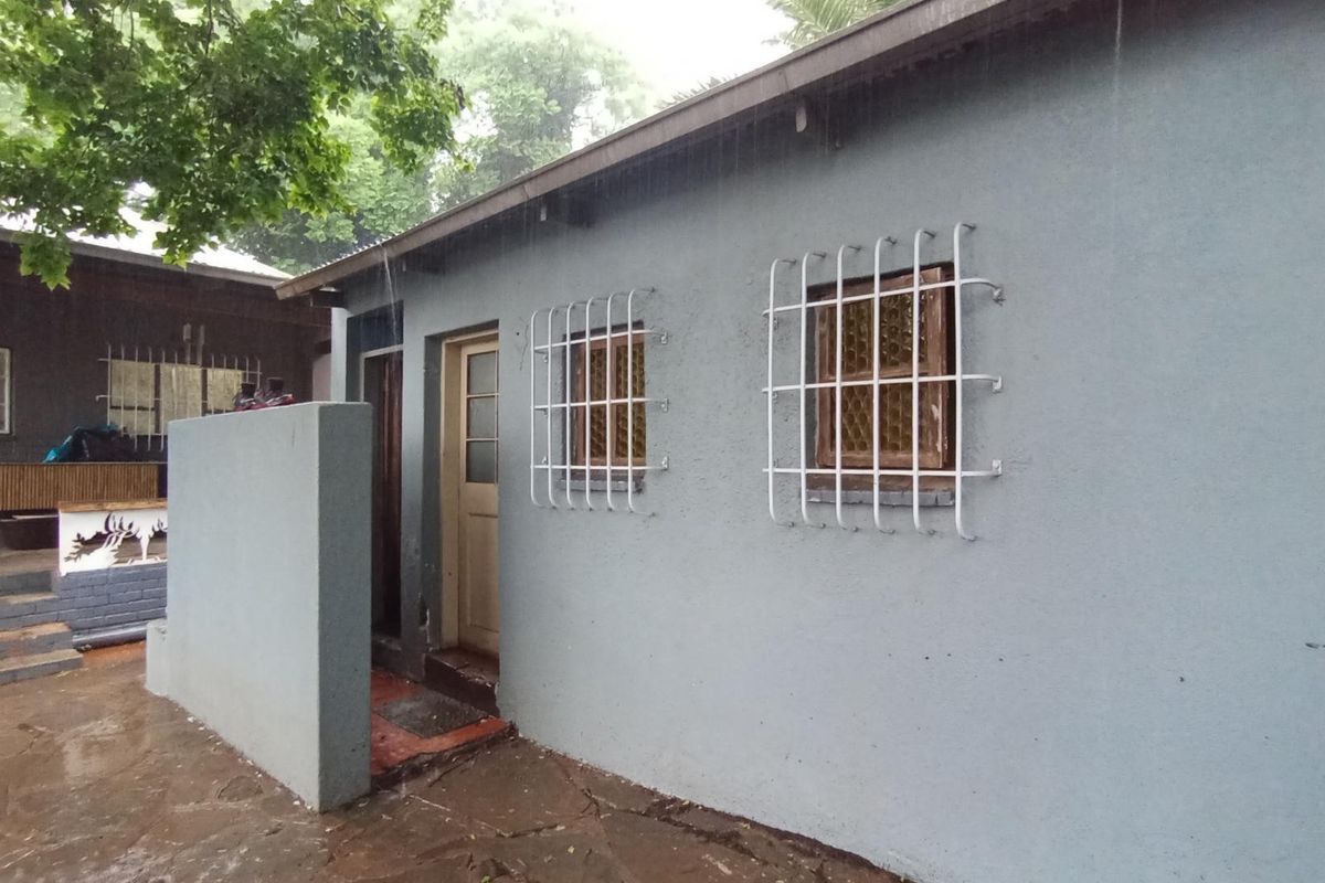 Rear exterior view of the property featuring a paved courtyard, concrete walls, and windows fitted with security bars.