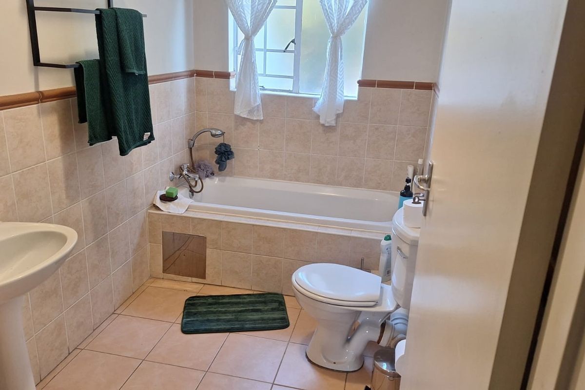 A functional bathroom featuring a pedestal basin, built-in bathtub, and toilet with neutral wall and floor tiling.