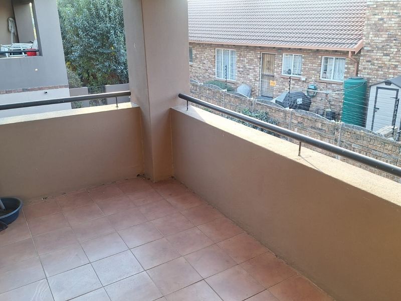 A covered balcony featuring tiled flooring and a metal balustrade, offering an outdoor space with views of the surrounding residential complex.