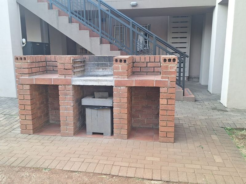 A communal outdoor area featuring a built-in brick braai facility set within a paved courtyard with access to an external staircase.