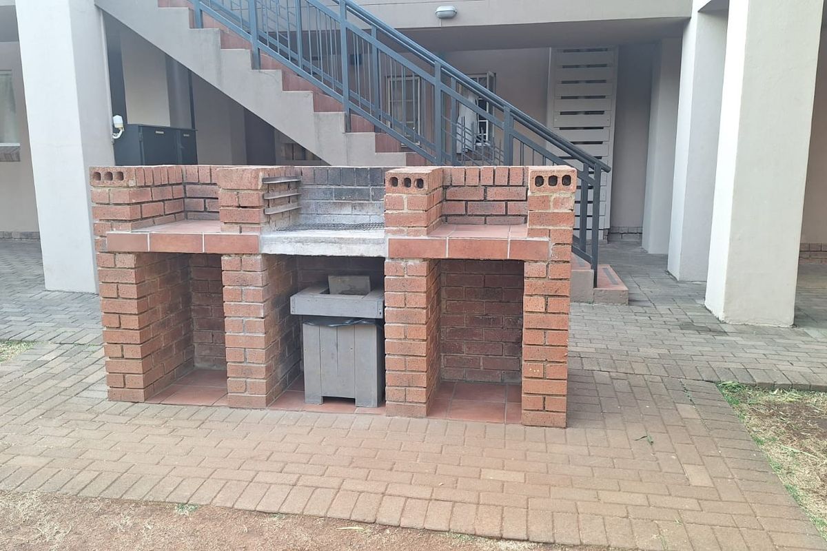 A communal outdoor area featuring a built-in brick braai facility set within a paved courtyard with access to an external staircase.