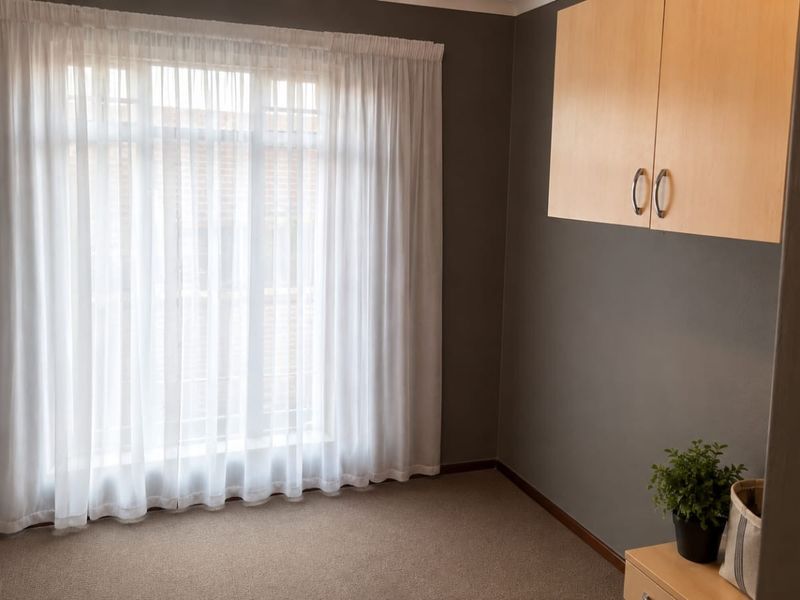 A clean, empty bedroom featuring neutral grey walls, carpeted flooring, and built-in overhead cabinetry, offering a versatile space ready for personalization.