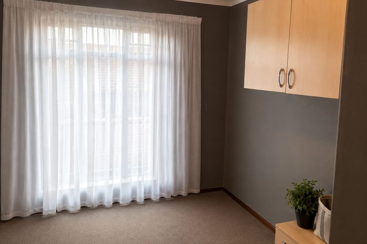 A clean, empty bedroom featuring neutral grey walls, carpeted flooring, and built-in overhead cabinetry, offering a versatile space ready for personalization.