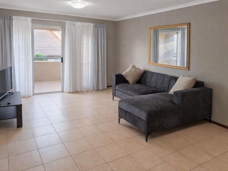 A well-maintained living room featuring neutral tiled flooring, cove cornicing, and a sliding glass door providing access to an outdoor balcony area.