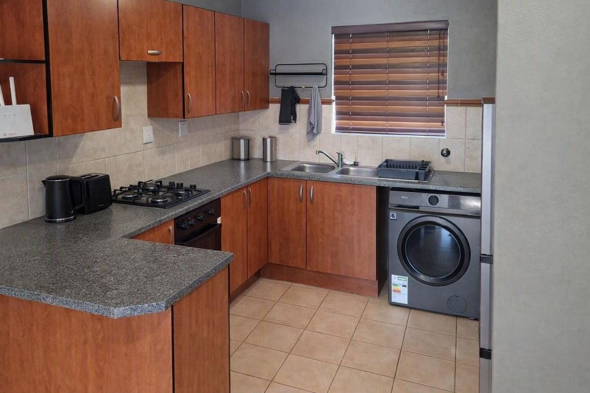 Functional kitchen featuring wood-finish cabinetry, granite-look countertops, a gas hob, built-in oven, and integrated laundry space with tiled flooring and splashbacks.