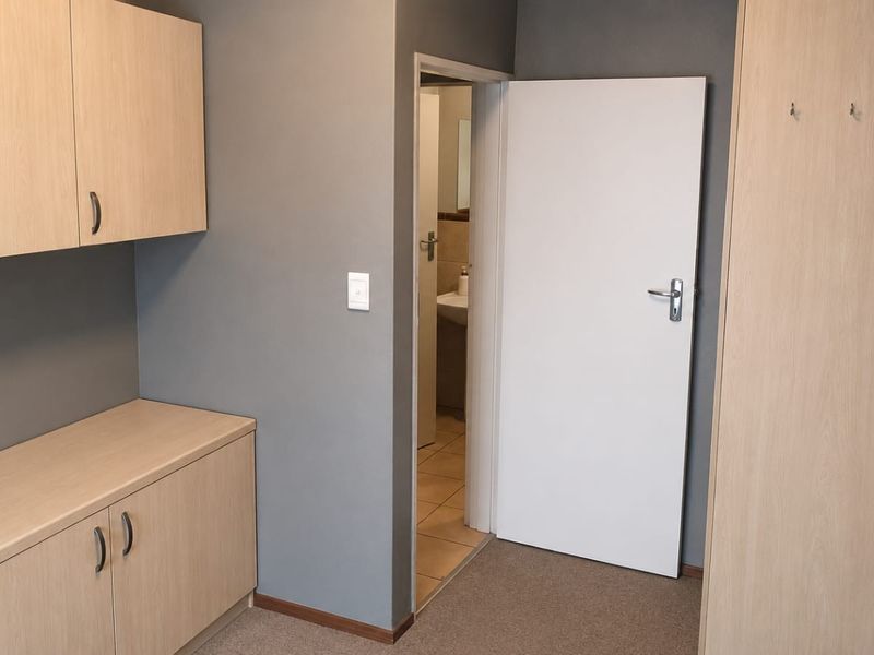 A clean hallway featuring built-in cabinetry, a tall wardrobe, and neutral grey walls, providing functional storage space with access to an adjacent bathroom.