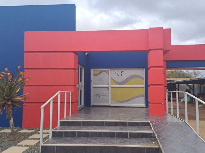 Front entrance of the office building featuring tiled steps, metal handrails, and a glass door with branded signage.