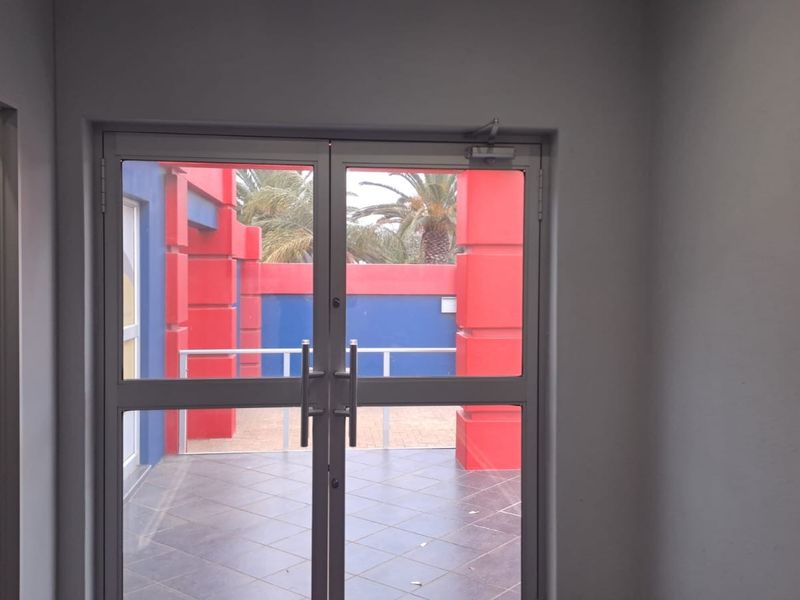 An empty office space featuring double glass doors that open onto an outdoor patio area with tiled flooring.