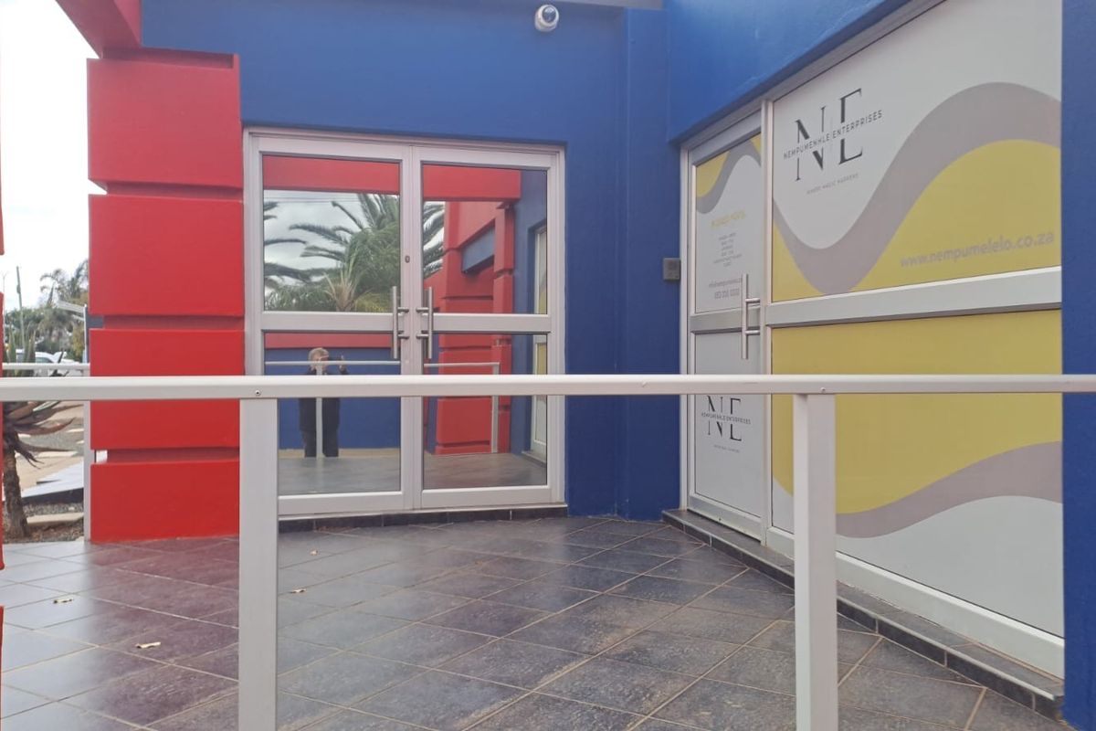 Front entrance of the office building featuring tiled landing, aluminium glass doors, and branded window decals.