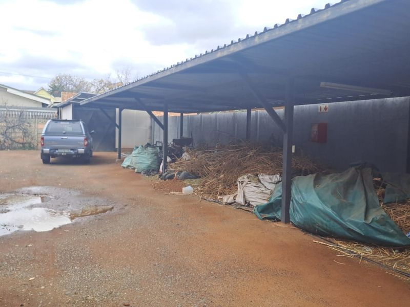 An outdoor carport area with a metal roof structure and concrete boundary wall, currently used for storage.