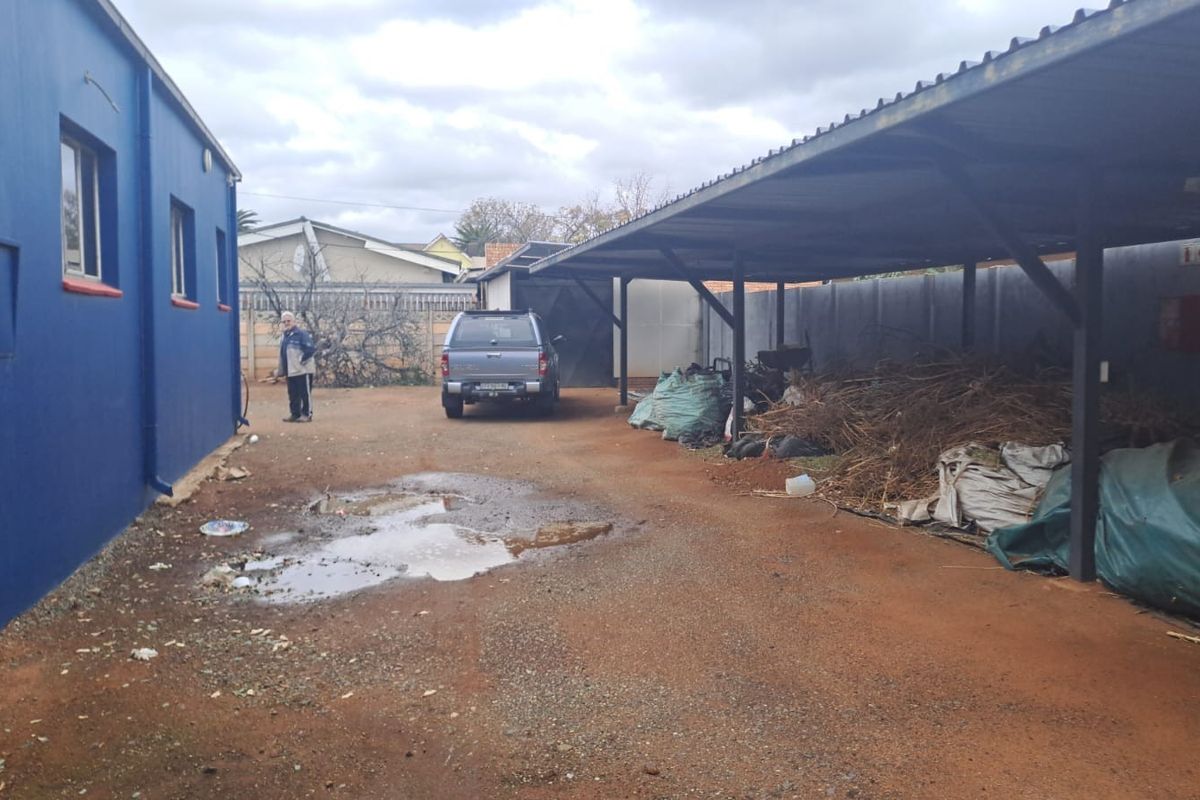 Rear exterior area of the office property featuring a large metal carport structure and unpaved ground surface.