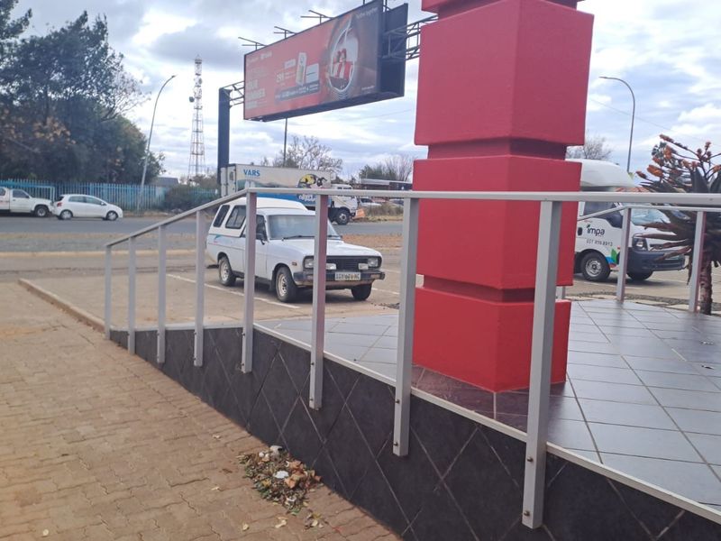 Exterior view of the office entrance featuring a tiled platform, metal handrail, and paved access area with a prominent billboard.