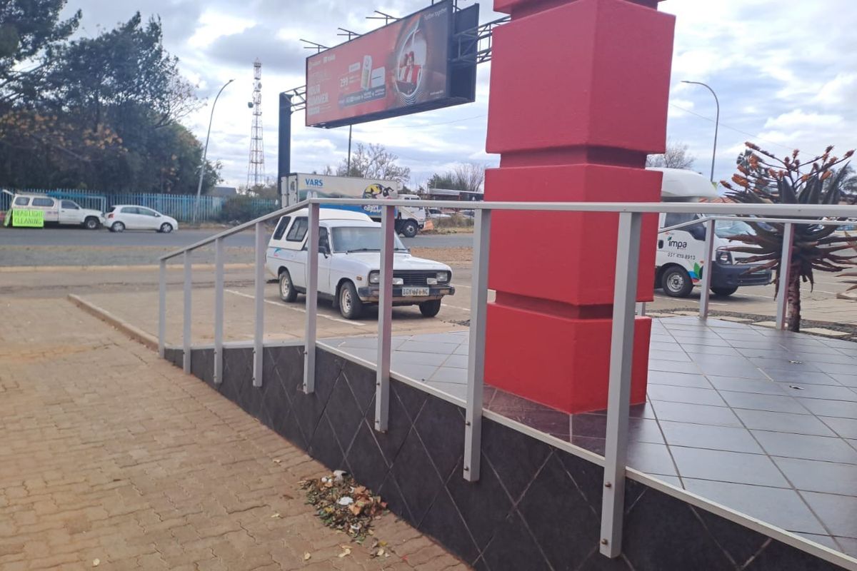 Exterior view of the office entrance featuring a tiled platform, metal handrail, and paved access area with a prominent billboard.