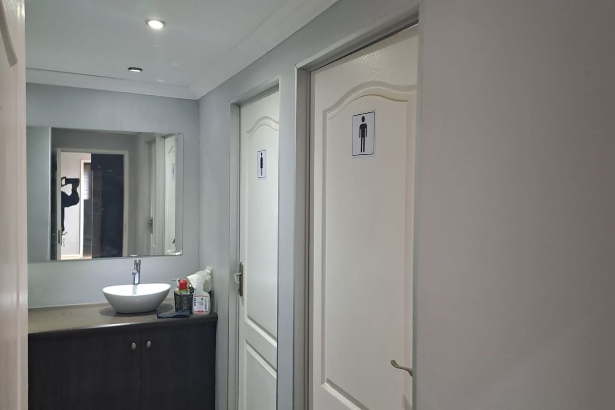 A clean office restroom area featuring a modern vessel sink vanity, large wall mirror, and separate male and female designated restroom doors.