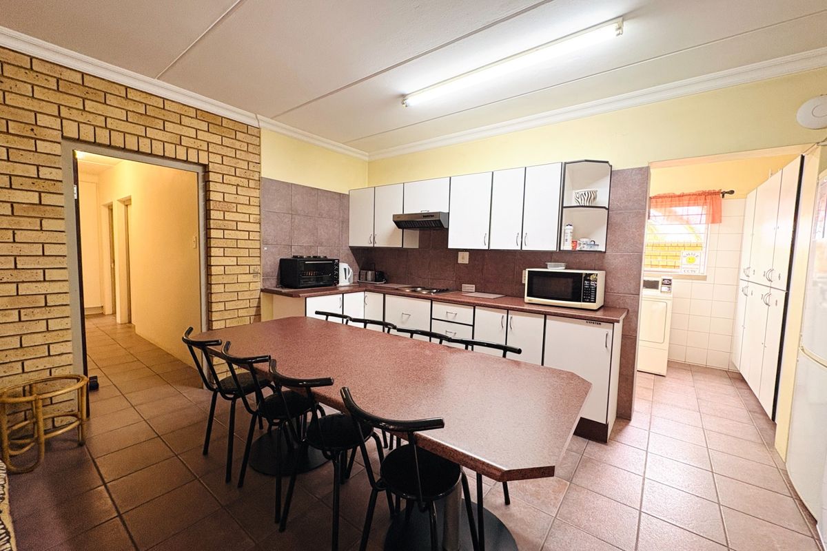 Functional kitchen featuring built-in cabinetry, tiled backsplash, and flooring, with an adjacent dining area and access to a separate laundry space.
