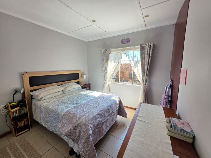 A functional bedroom featuring tiled flooring, a built-in cupboard, and natural light through a window.