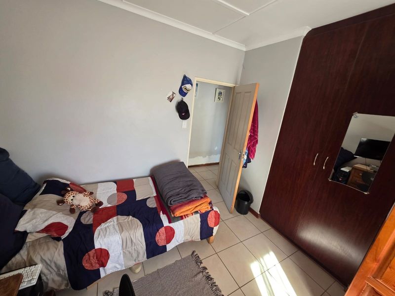 A bedroom featuring tiled flooring, a built-in dark wood wardrobe, and coved ceiling detailing, with an open doorway leading to an adjacent space.