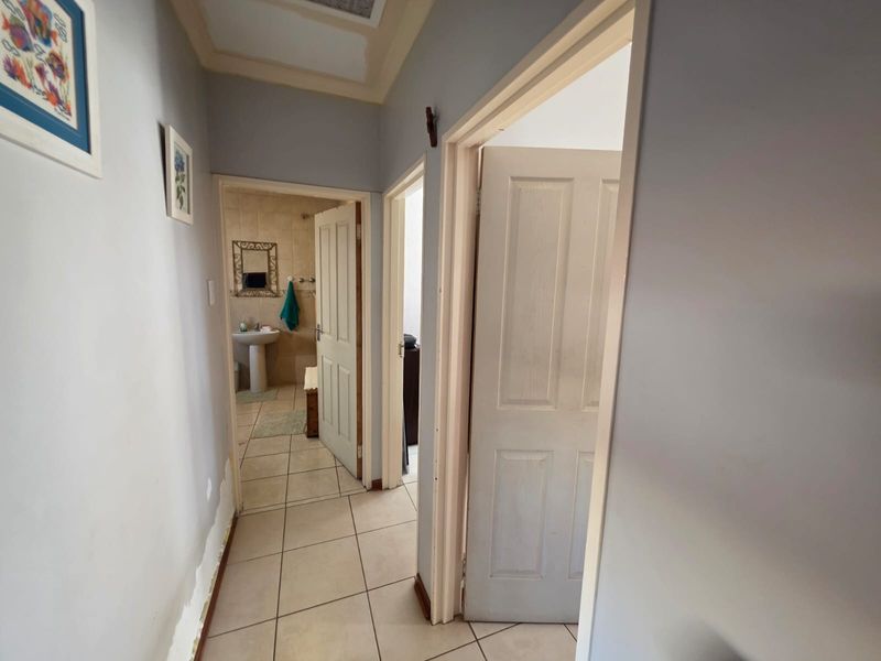 A hallway with tiled flooring leading to a bathroom, showing visible wear and damage to the lower wall sections requiring repair.