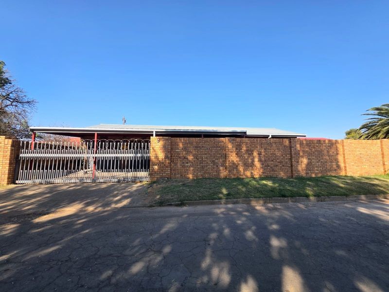 Front exterior view of the property featuring a brick boundary wall, metal security gate, and a covered carport area.