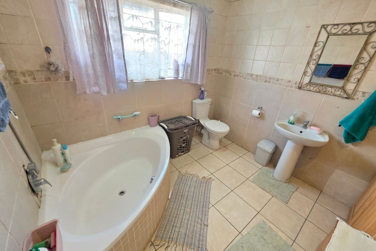 A functional bathroom featuring a corner bathtub, pedestal sink, and toilet with neutral wall and floor tiling.