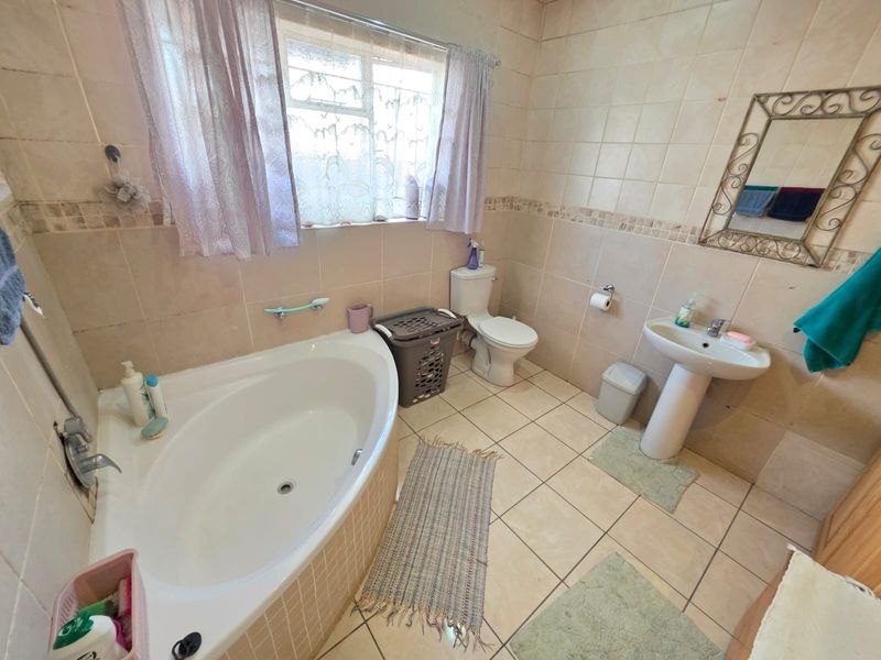 A functional bathroom featuring a corner bathtub, pedestal sink, and toilet with neutral wall and floor tiling.