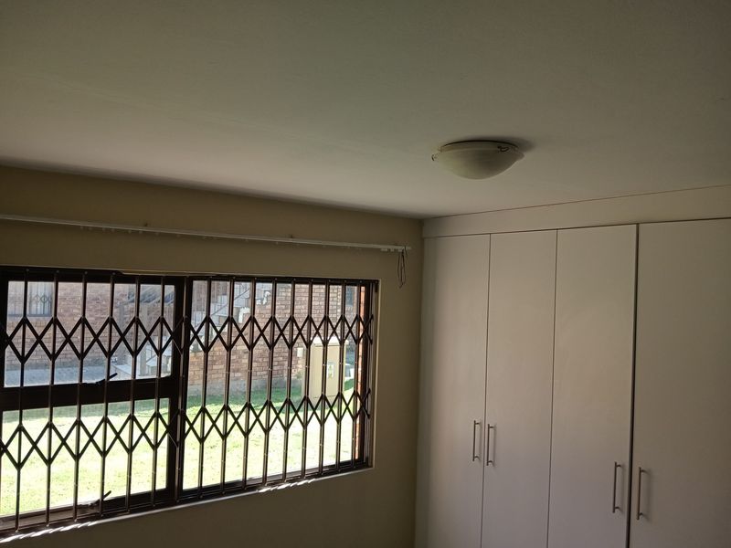 A bedroom featuring built-in cupboards and a window fitted with a security gate, offering a functional and secure living space.