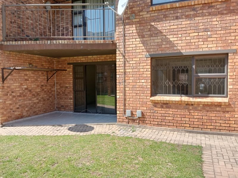Rear view of a face brick apartment building featuring a ground floor paved patio, sliding door access, and an upper-level balcony with metal railings.