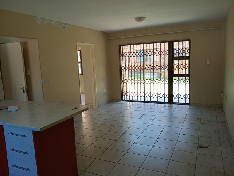 Open-plan living area featuring tiled flooring, a kitchen island with built-in cabinetry, and a security gate leading to the exterior.