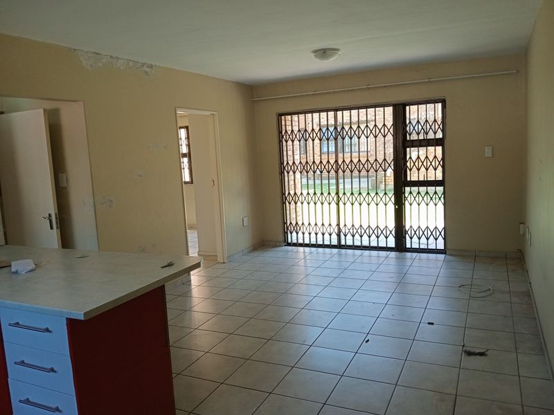 An open-plan living area featuring tiled floors, a kitchen island, and a sliding door with a security gate leading to the exterior.