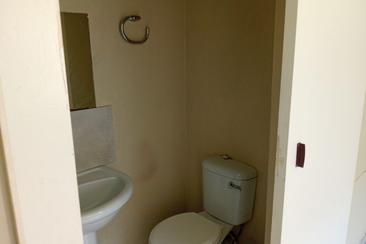A compact guest bathroom featuring a pedestal basin, toilet, and wall-mounted mirror, requiring minor cosmetic updates to refresh the space.