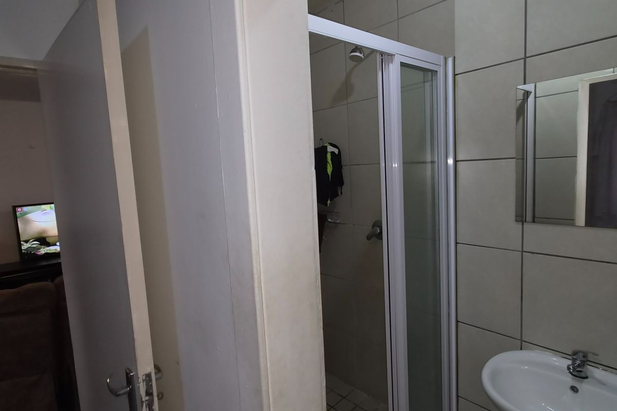 A functional bathroom featuring a shower enclosure, wall-mounted basin with mixer tap, and tiled wall finishes.