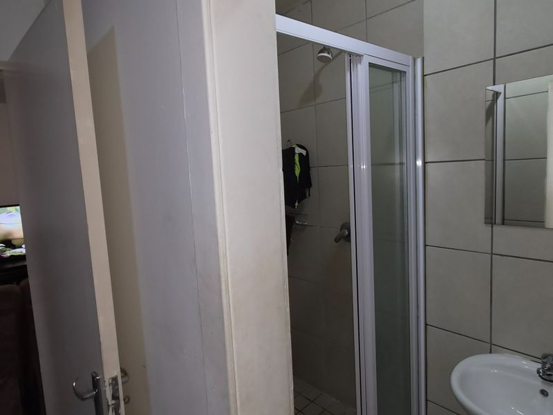 A functional bathroom featuring a shower enclosure, wall-mounted basin with mixer tap, and tiled wall finishes.