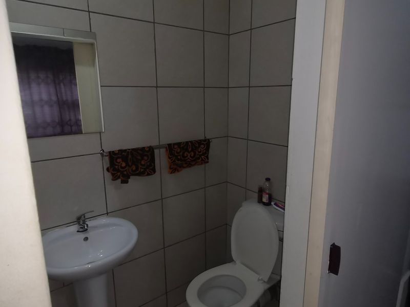 A compact bathroom featuring a pedestal basin, toilet, and full-height wall tiling.