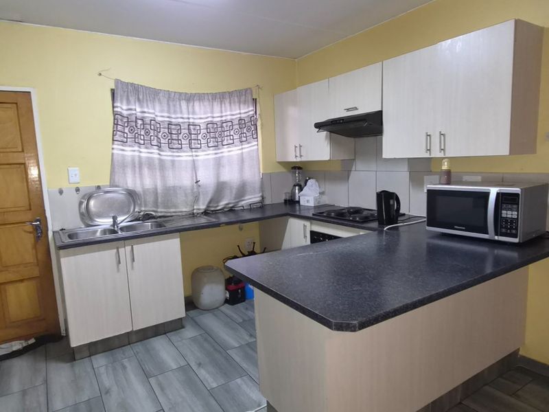 Functional kitchen featuring laminate cabinetry, dark countertops, built-in hob with extractor fan, and tiled flooring.