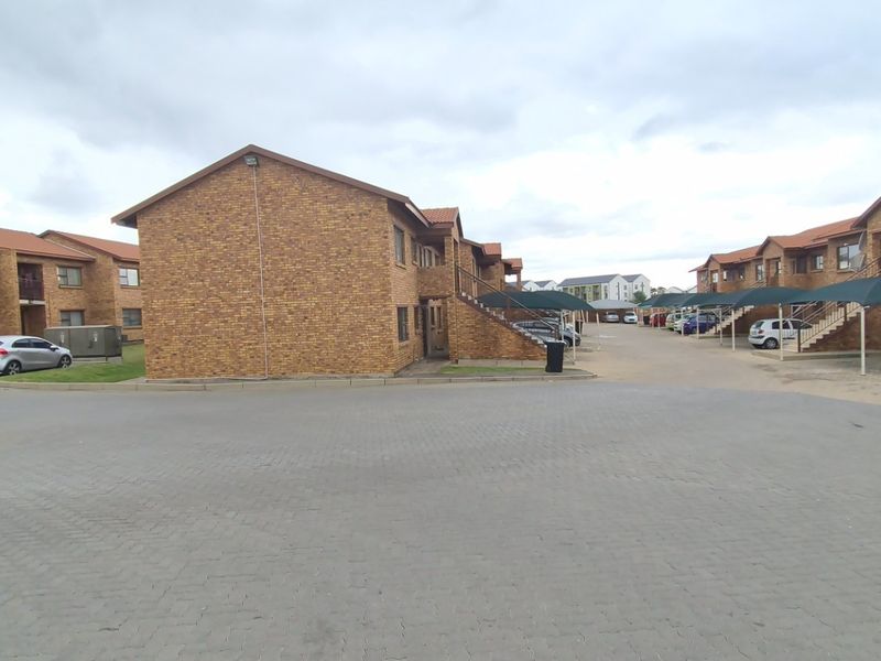 Exterior view of a multi-unit apartment complex featuring face-brick facades, tiled roofs, paved parking areas, and covered carports.