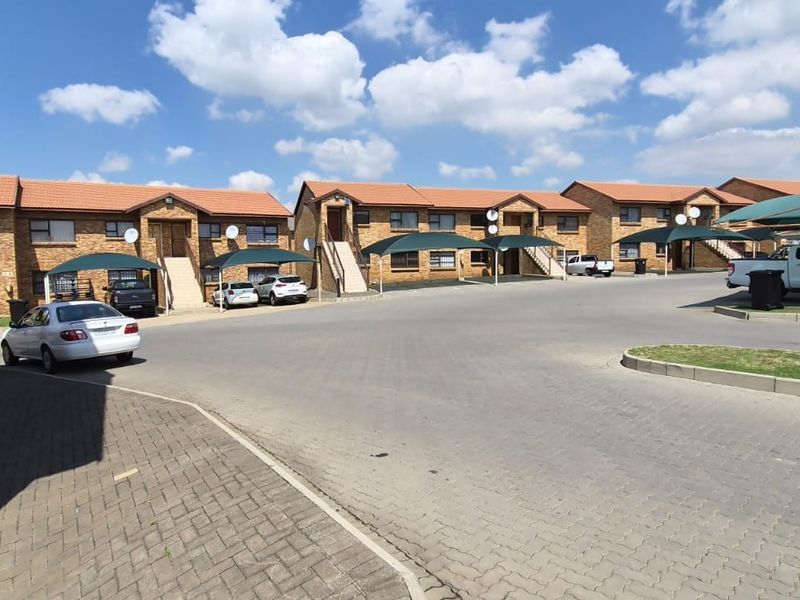Exterior view of a residential apartment complex featuring brick facades, tiled roofs, and dedicated shade cloth parking bays for residents.