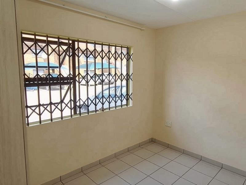 An empty bedroom featuring tiled flooring, a built-in cupboard, and a window fitted with a security gate.
