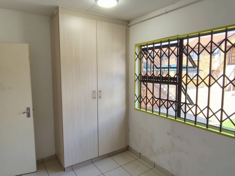 An empty bedroom featuring tiled flooring, a built-in wardrobe, and a window fitted with a security gate.