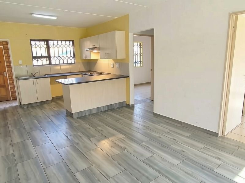 Open-plan living area featuring a functional kitchen with built-in cabinetry, hob, extractor fan, and modern laminate flooring throughout the space.